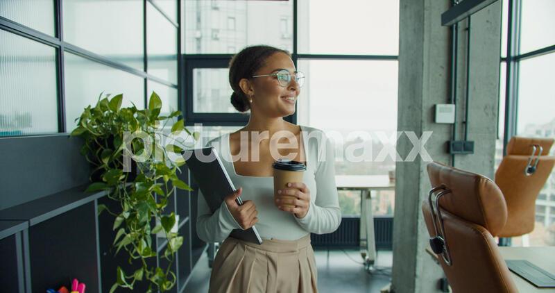 a confident young woman in an elegant outfit, holding a coffee cup and laptop, walking through a bright modern office space with large windows, stylish furniture, and green plants, 9.43 MB, <<>> MB1