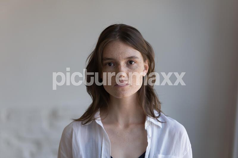 Serious pretty freckled young woman front head shot indoor portrait. Student teenage girl, female model with spotted facial skin wearing casual, posing at home, looking at camera